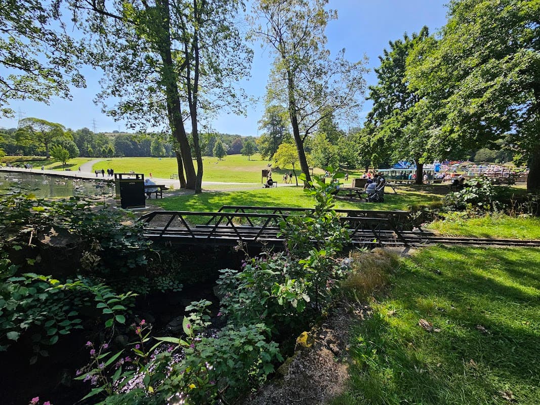 View of Mereside Car Park with greenery, trees, and people enjoying a sunny day in Halifax, Yorkshire.