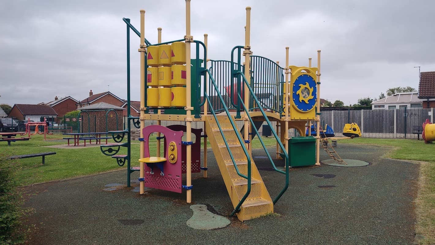 Colorful playground equipment with slides, climbing structures, and play panels set in a grassy area.