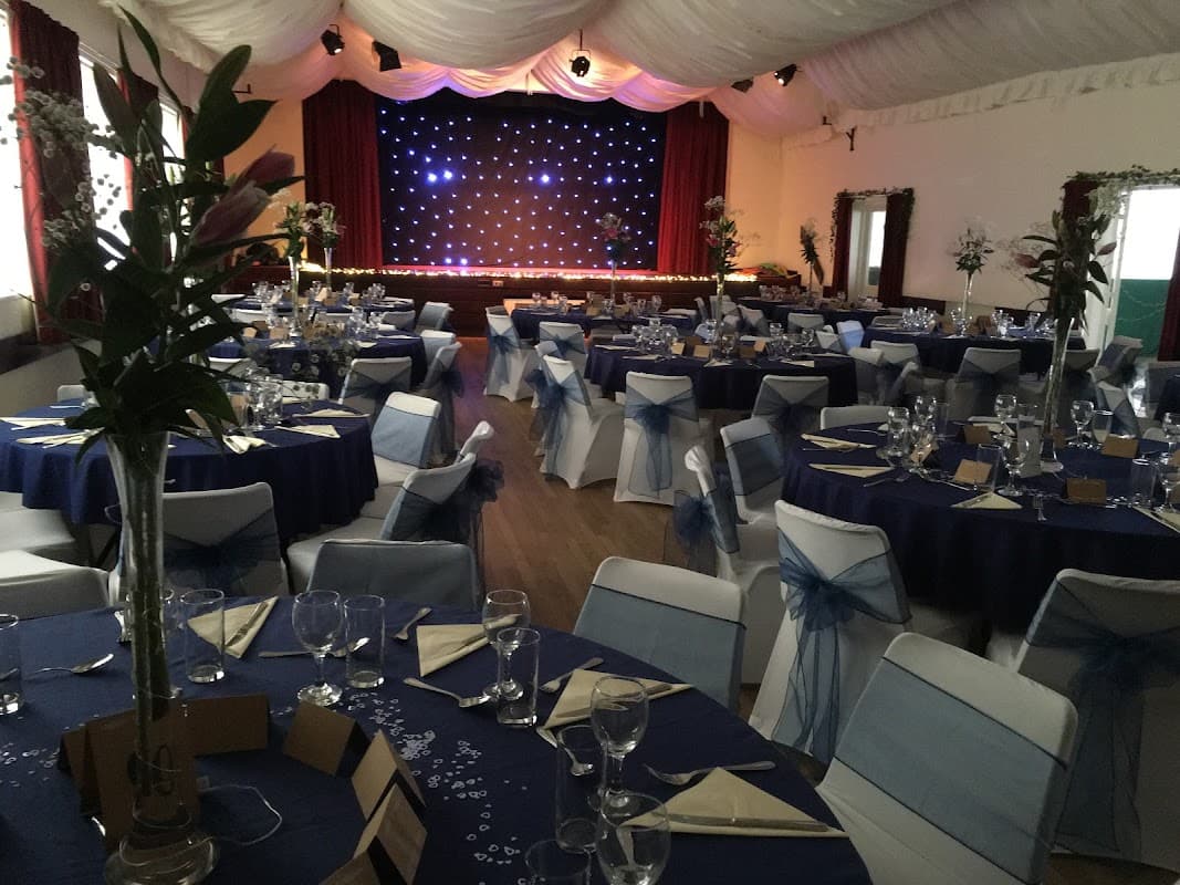 Elegant event space with round tables, blue and white decor, and a stage with twinkling lights in Hampsthwaite Memorial Hall.