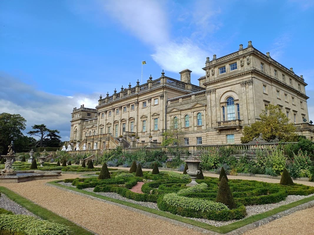 Harewood House with intricate gardens, manicured hedges, and a blue sky in the background.