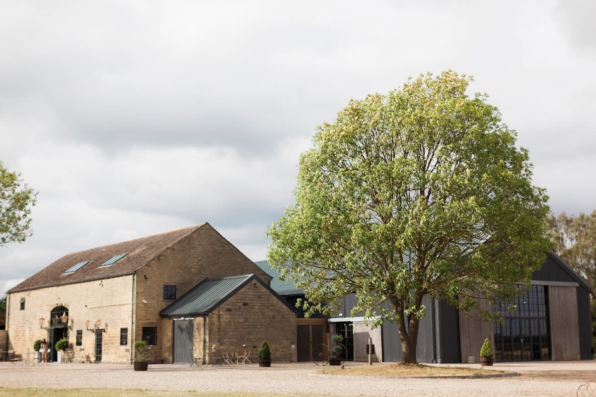 Stone buildings with large windows, a lush green tree, and a cloudy sky at Wharfedale Grange in Harewood, Yorkshire.