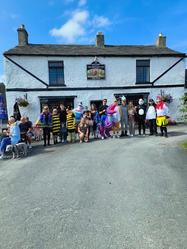 Group of people in colorful costumes outside Pheasant Inn & Caravan Park, with a clear blue sky and flowers.