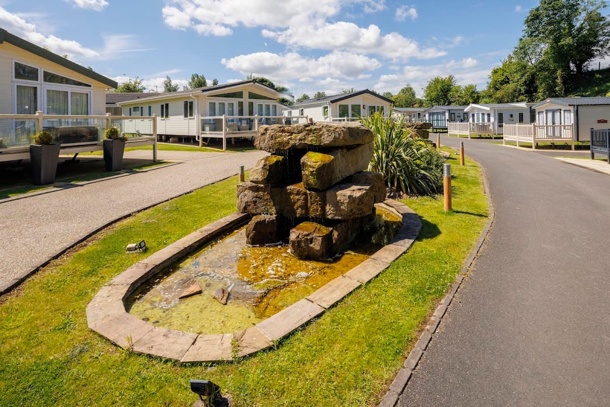 A landscaped holiday park featuring a stone fountain, neatly arranged homes, and a sunny sky in Yorkshire.