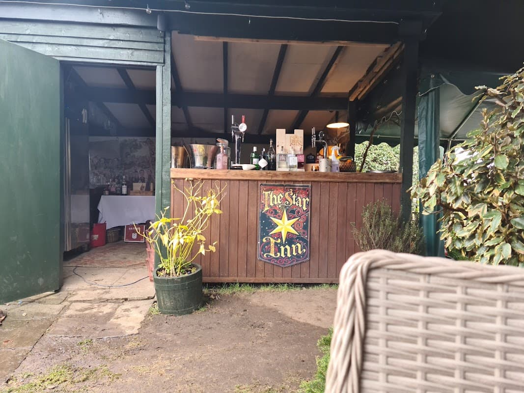 Wooden bar with "The Star Inn" sign, plants in pots, and a cozy outdoor seating area in a rustic setting.