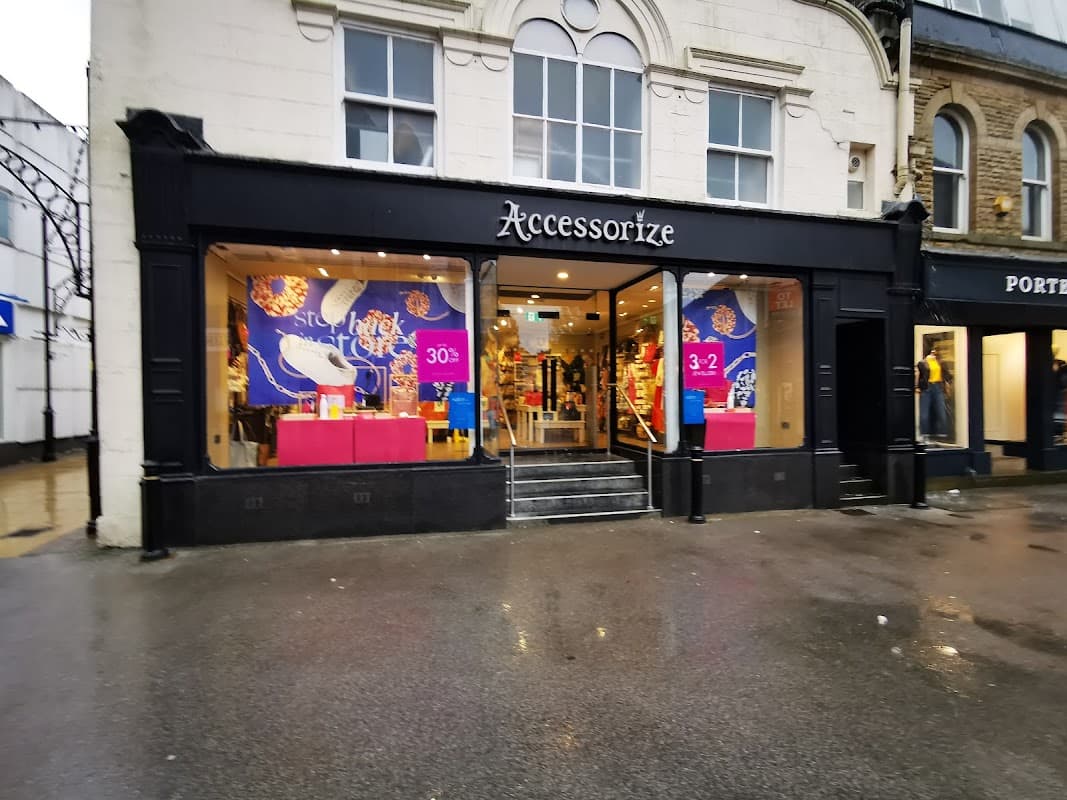 Storefront of Accessorize with colorful displays and signage, featuring promotions and a wet pavement outside.