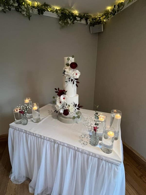 Elegant three-tier cake adorned with flowers and greenery, surrounded by lit candles on a draped table.