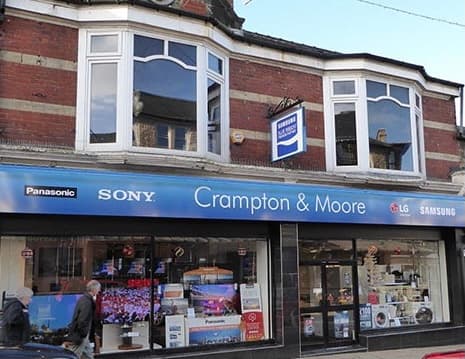 Bookshop storefront with large windows, signage for "Crampton & Moore," and various electronic brands displayed.