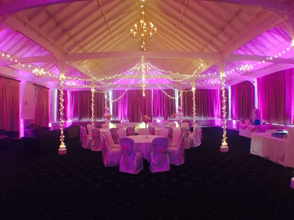 Elegant event space with round tables, white chair covers, and purple lighting, adorned with string lights and chandeliers.