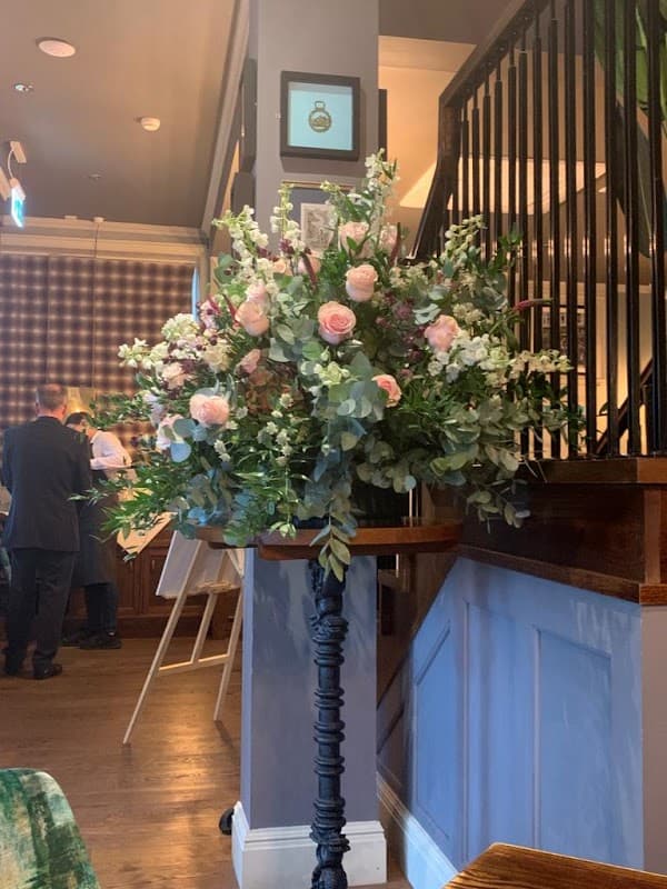 Elegant floral arrangement featuring pink roses and greenery, displayed on a decorative stand in a stylish interior.