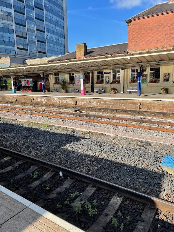 Harrogate Station platform with waiting area, train tracks, and nearby buildings under a clear blue sky.