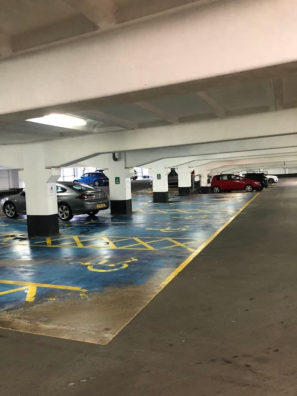 Empty car park with marked spaces, concrete pillars, and parked cars under bright overhead lighting.