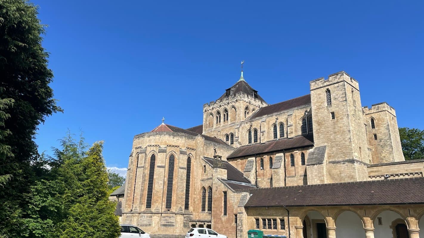 St. Wilfrid's Church features stone architecture, a tall steeple, and surrounding greenery under a clear blue sky.