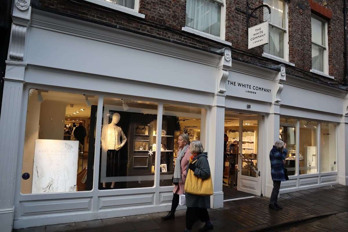 The White Company storefront featuring elegant displays, mannequins, and shoppers in a charming street setting.