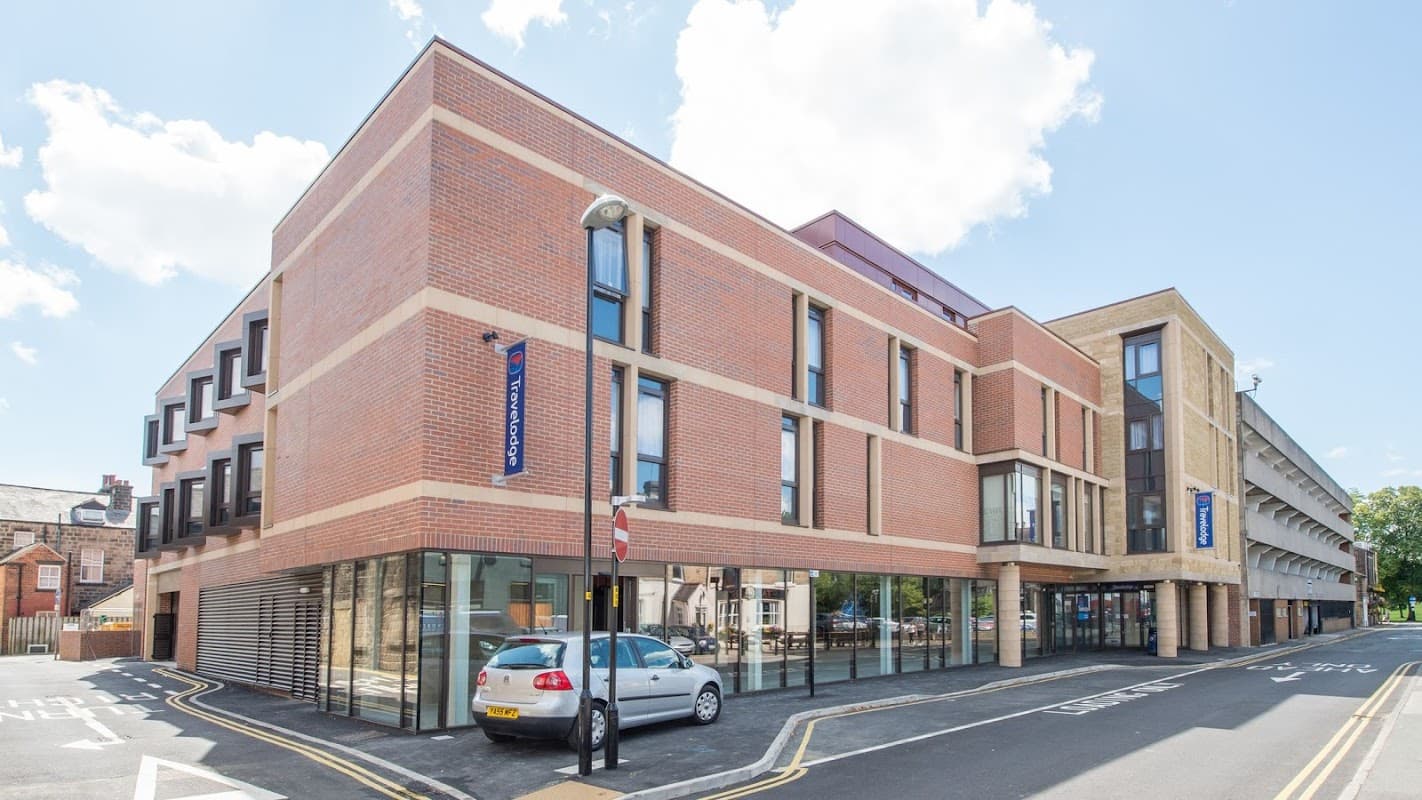 Modern brick building with large windows, featuring a Travelodge sign, located on a street in Harrogate, Yorkshire.