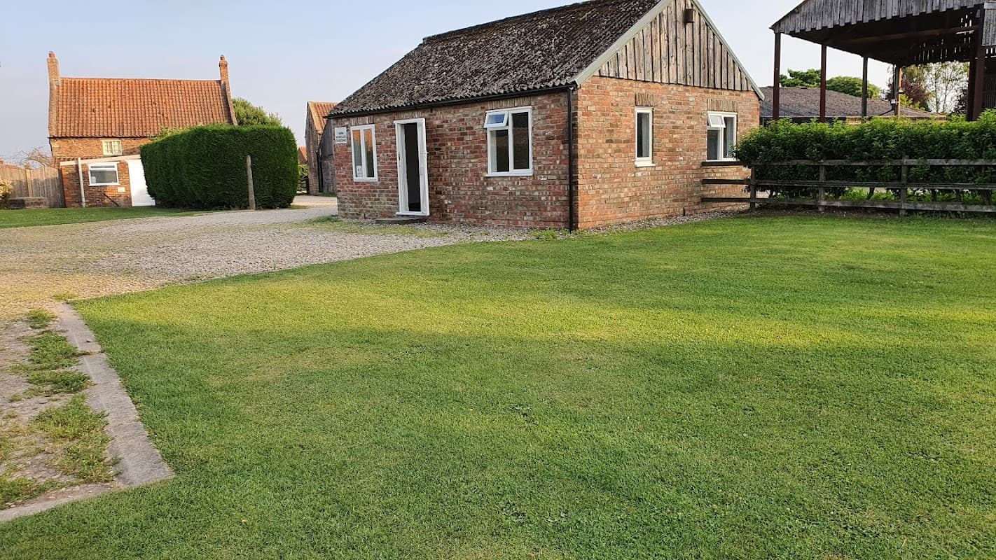 Brick building with a thatched roof, surrounded by green grass and trees, set in a peaceful rural area.