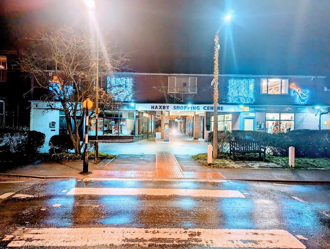 Haxby Shopping Centre entrance illuminated at night, with decorative lights and a wet pavement reflecting the glow.