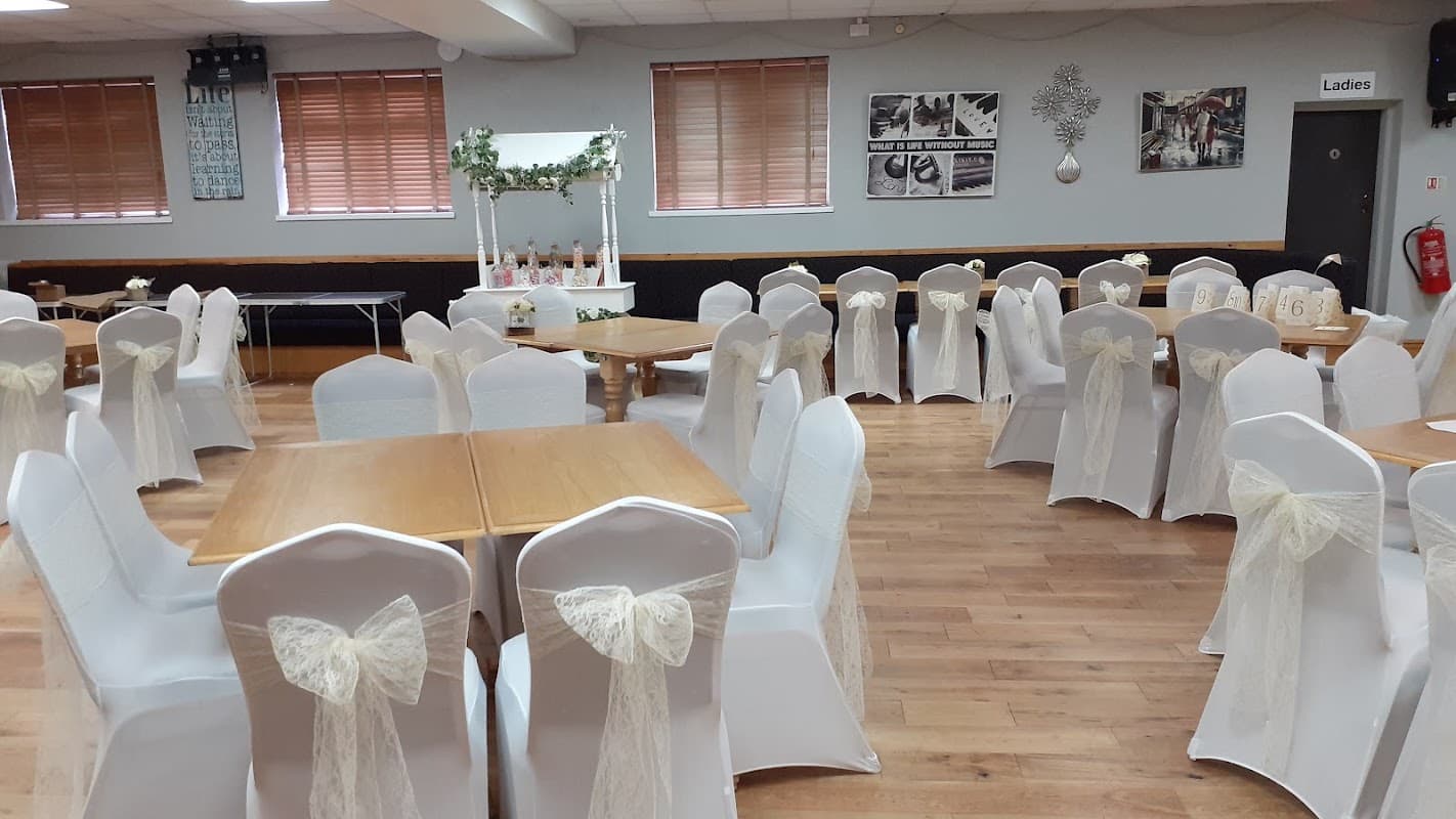 Decorated dining area with tables and white chairs adorned with bows, wooden flooring, and wall decorations.