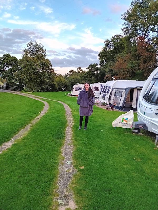 A woman in a purple coat stands on a grassy path beside parked caravans at Low Wood Caravan Park.