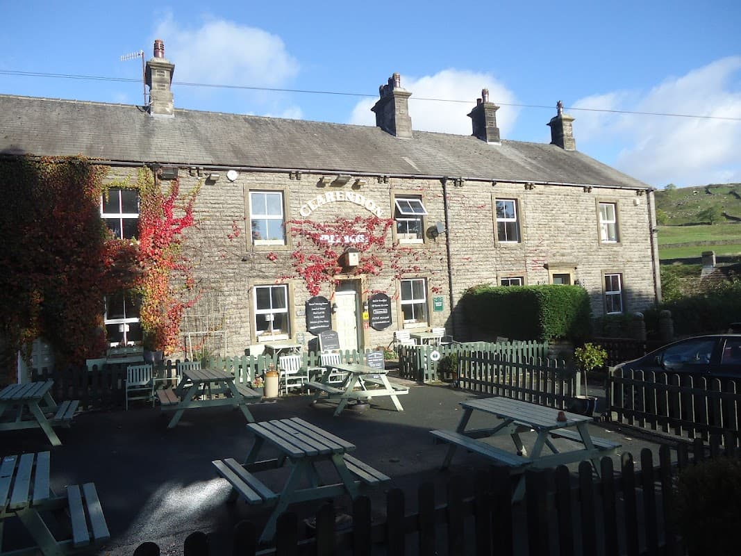 Historic stone building with ivy, outdoor seating, and a sign reading "Clarendon Hotel" against a blue sky.