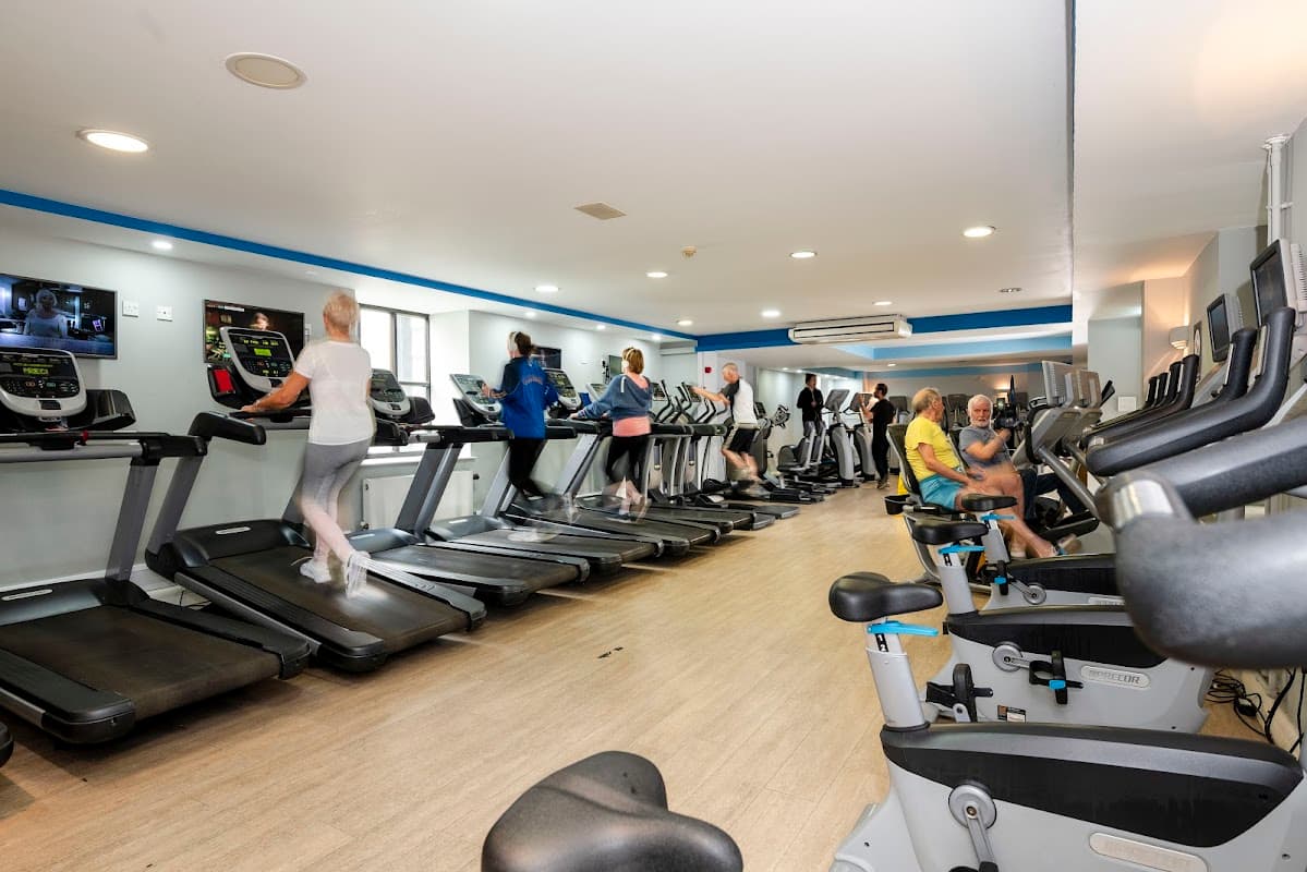 Fitness enthusiasts using treadmills and exercise bikes in a bright gym with modern equipment and large windows.