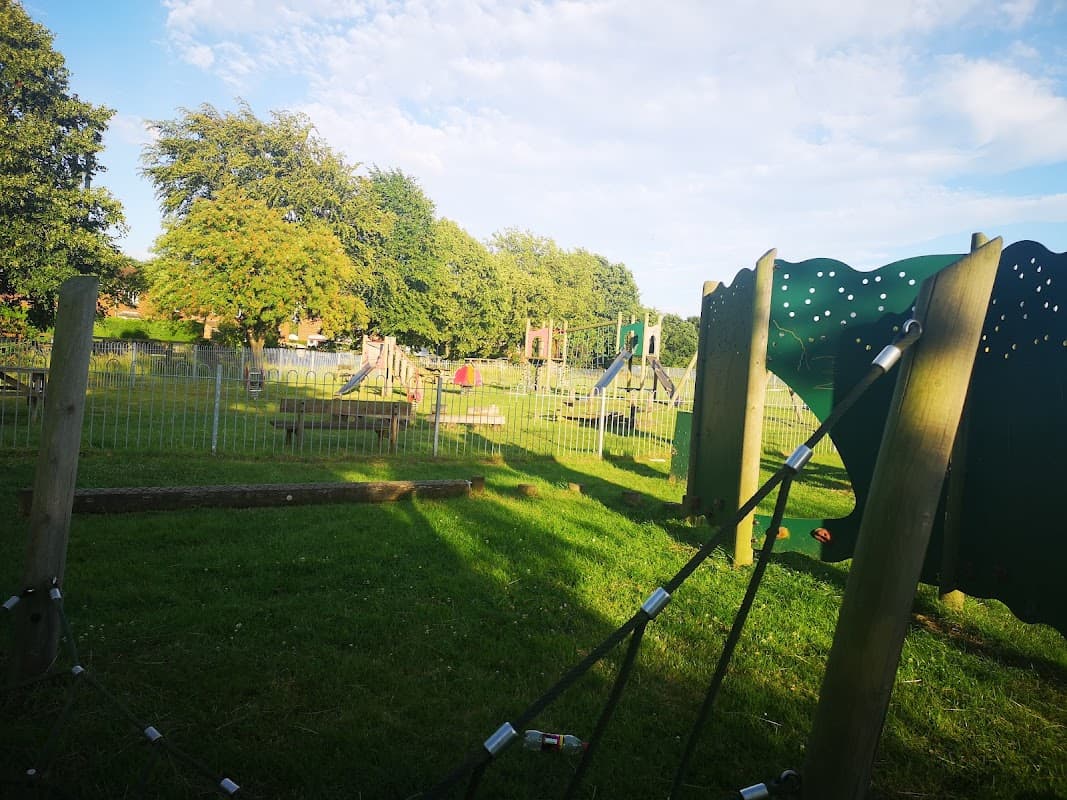 Playground in Hemingbrough with climbing frames, swings, and grassy areas under a blue sky with scattered clouds.