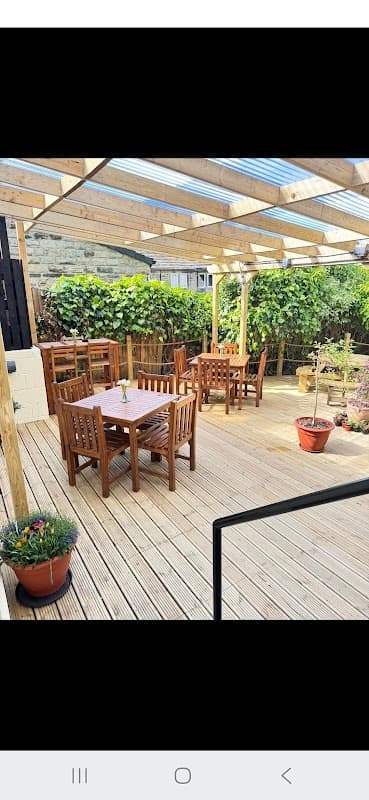 Wooden outdoor seating area with tables and chairs, surrounded by greenery and potted plants at The Butchers Arms.
