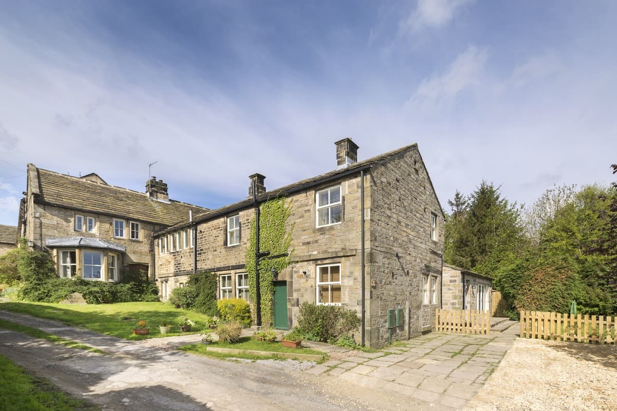 Stone-built hotel with ivy-covered walls, surrounded by greenery and a gravel path leading to a wooden fence.