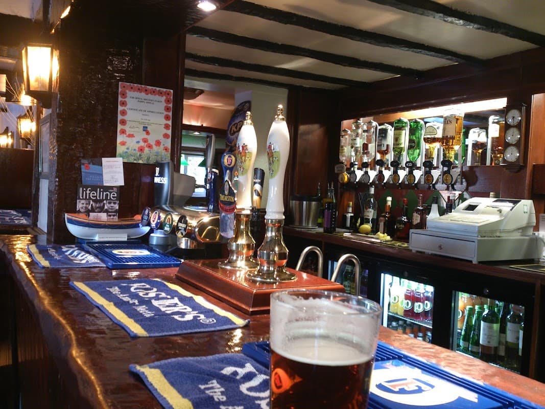 Wooden bar with beer taps, bottles, and a glass of beer in the foreground, creating a cozy pub atmosphere.