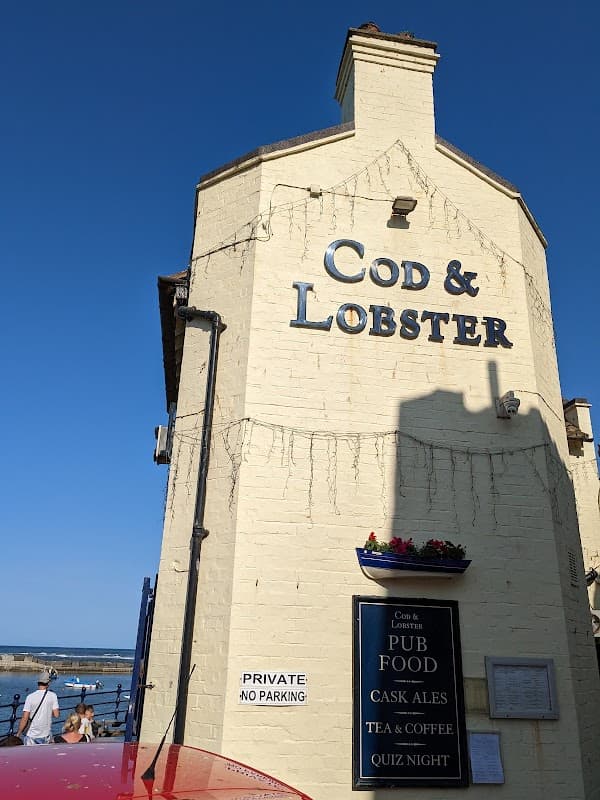 Exterior of Cod & Lobster pub with signage, a red vehicle, and a view of the sea in Hinderwell, Yorkshire.