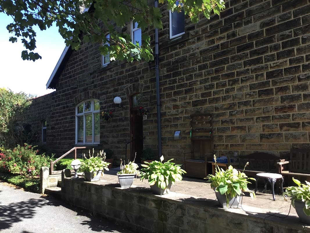 Stone exterior of The Firs Guesthouse with potted plants and a wooden bench on a sunny day in Hinderwell, Yorkshire.