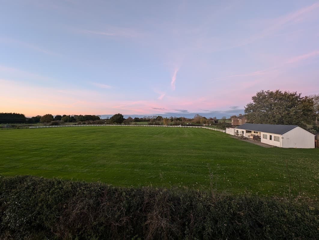 Cricket pitch with lush green grass, a white building, and a pastel sky at sunset in Hirst Courtney, Yorkshire.