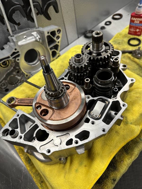 Engine components, including gears and a shaft, arranged on a yellow cloth with tools in the background.
