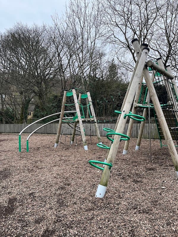 Playground equipment with climbing structures and slides, surrounded by wood chips and bare trees in Holme Valley.