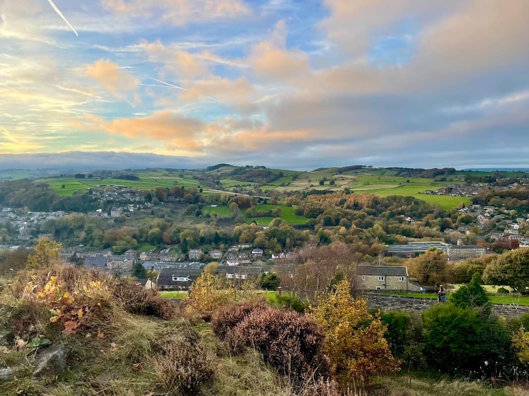Lush green hills and valleys under a colorful sky, with a quaint village nestled below in Holmfirth, Yorkshire.