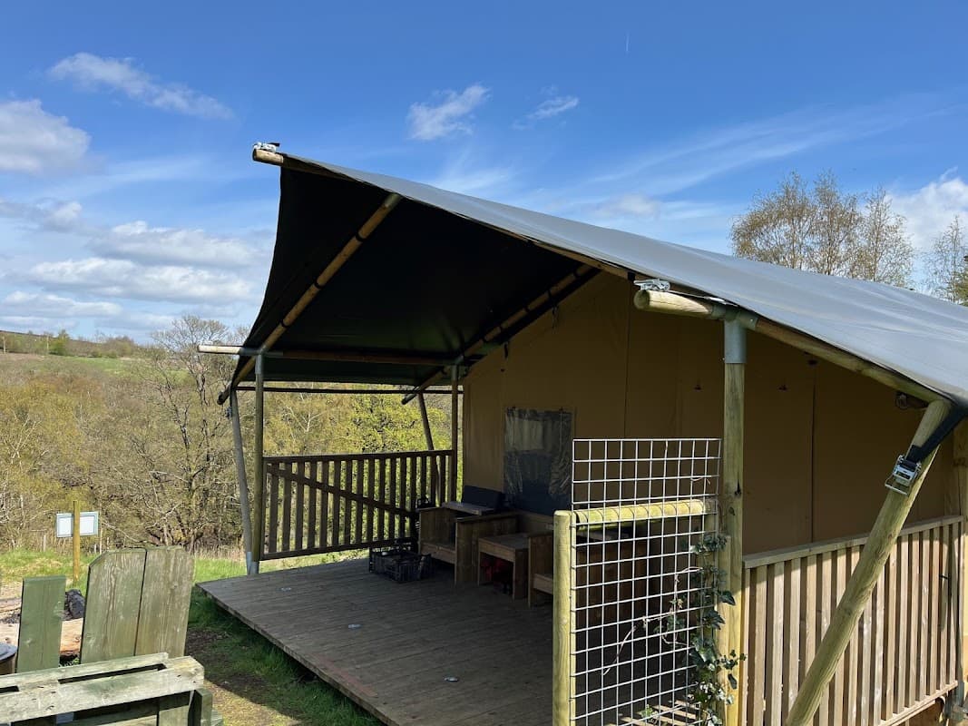 Glamping tent with a wooden deck, surrounded by trees and a blue sky in Secret Valley Escapes, Holme Valley.