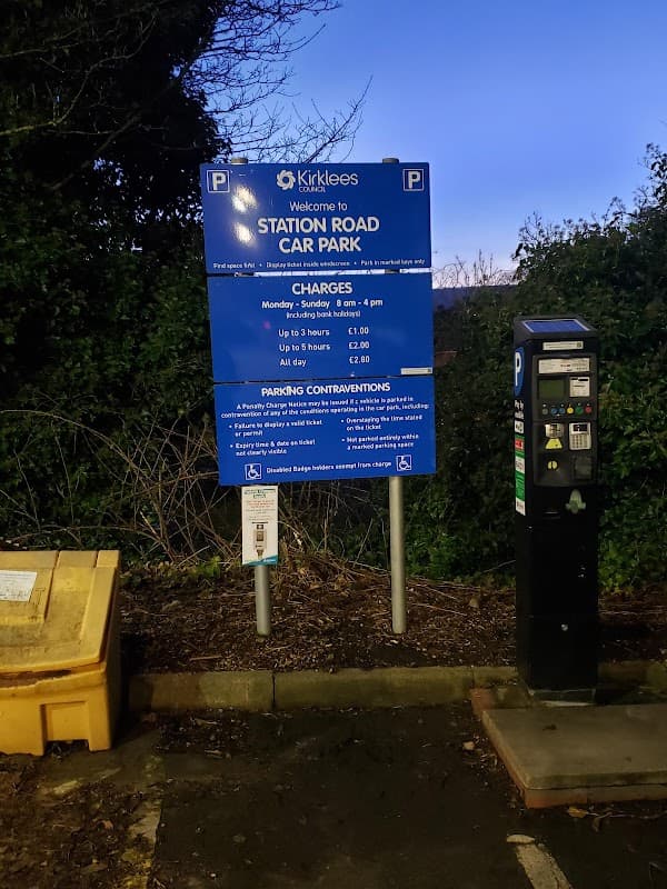 Sign for Station Road Car Park with parking fees, hours, and payment machine in Holme Valley, Yorkshire.
