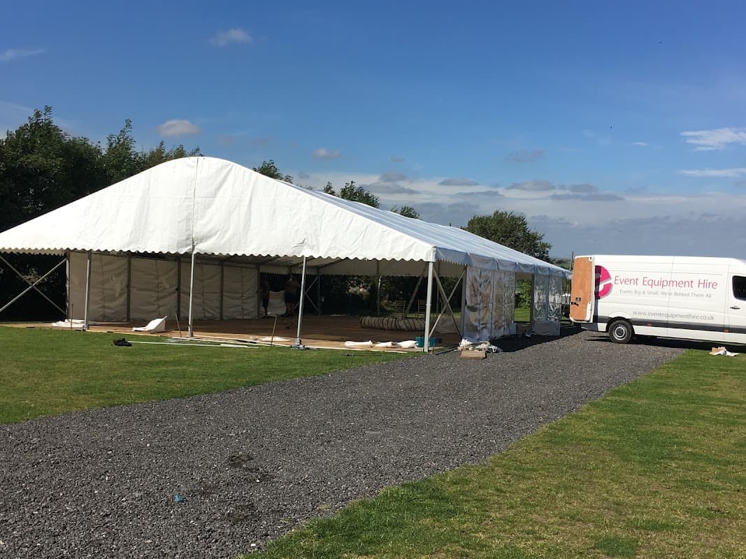 Large white marquee set up on a grassy area, with a delivery van parked nearby under a blue sky.