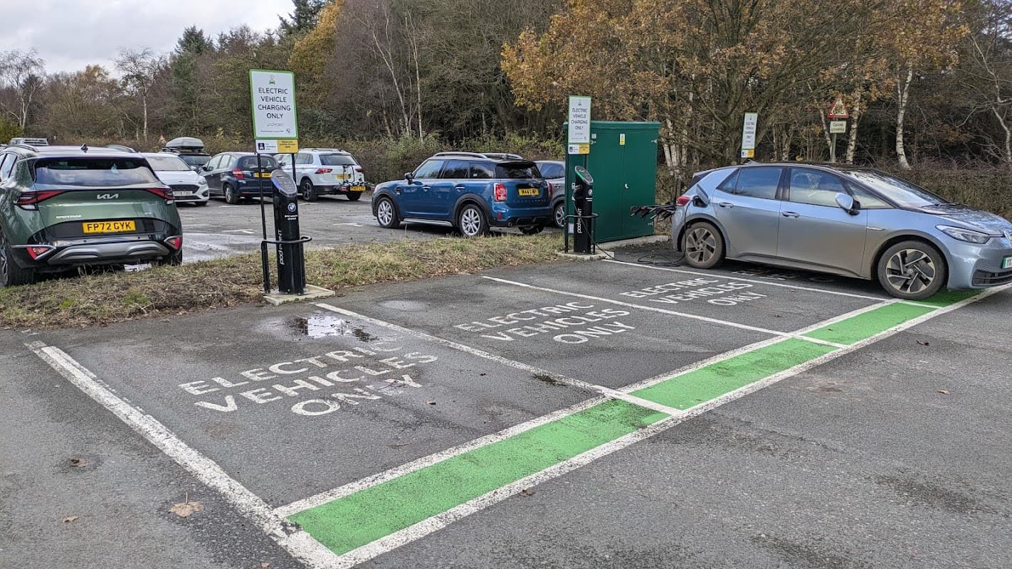 Pod Point Charging Station with designated electric vehicle parking spaces and signage in a wooded area.