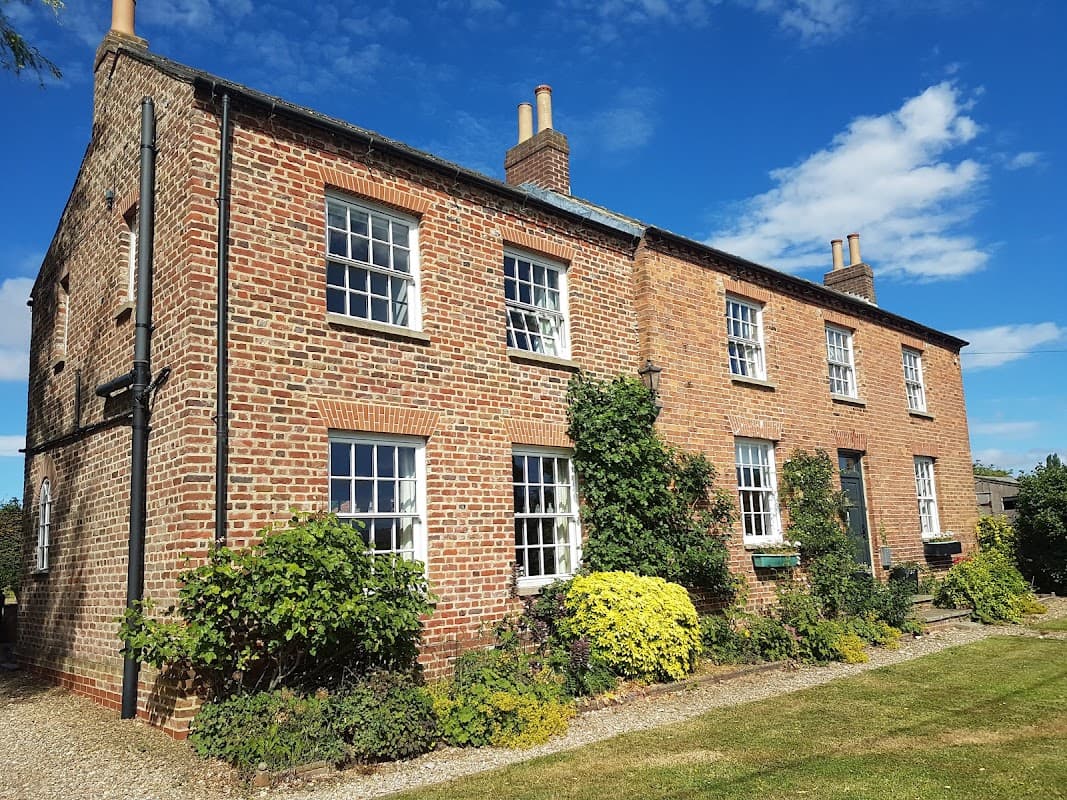 Charming brick hotel with multiple windows, surrounded by greenery and a clear blue sky in Hopperton, Yorkshire.