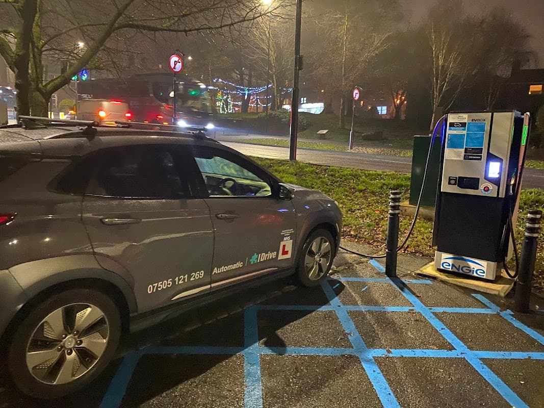 A grey car parked in a designated space near an electric vehicle charging station at night.