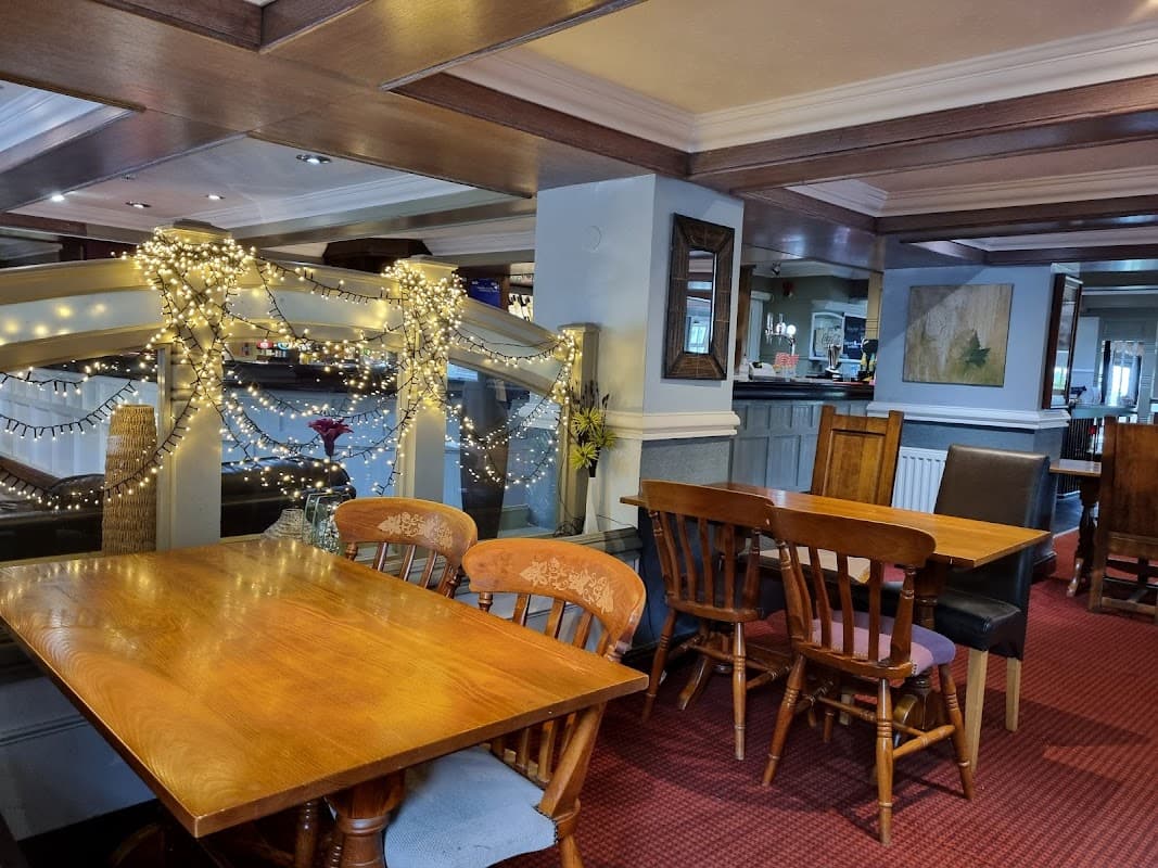 Cozy pub interior with wooden tables, chairs, and festive lights, featuring a bar and artwork on the walls.