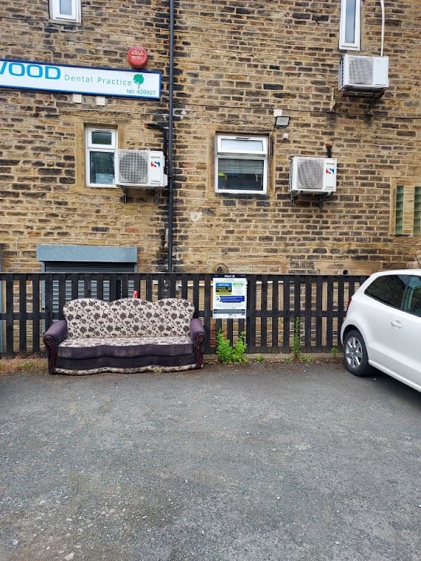 A parked white car beside a brown sofa with floral upholstery in front of a stone building with air conditioning units.