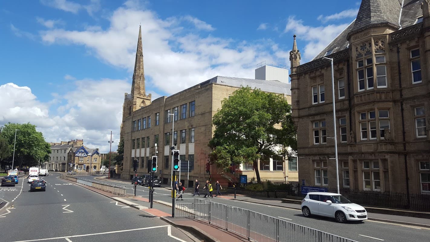 Pay & Display car park in Huddersfield, with historic buildings, traffic lights, and a clear blue sky.