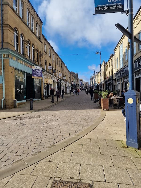Bustling street scene with shops, pedestrians, and blue sky in Huddersfield, Yorkshire.