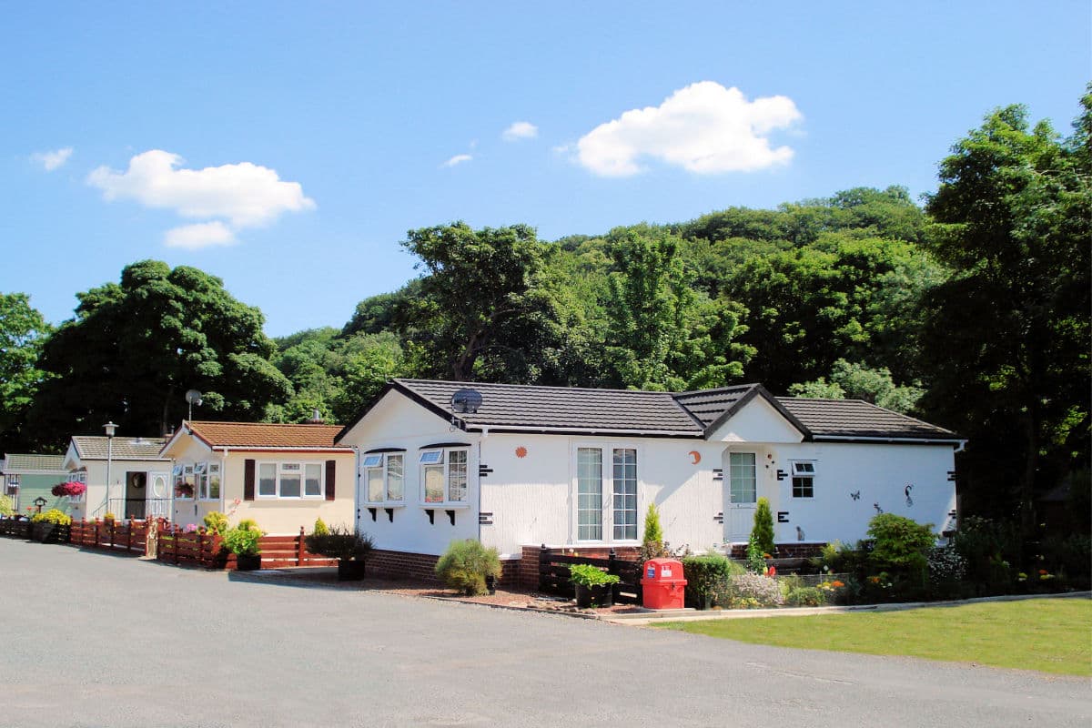 Caravans lined along a paved path, surrounded by trees and blue sky with fluffy clouds in Richmond Caravan Park.