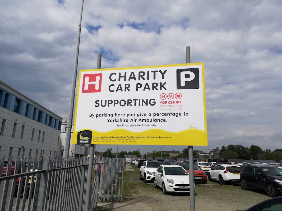 Sign for Charity Car Park supporting Yorkshire Air Ambulance, with parked cars and a cloudy sky in the background.