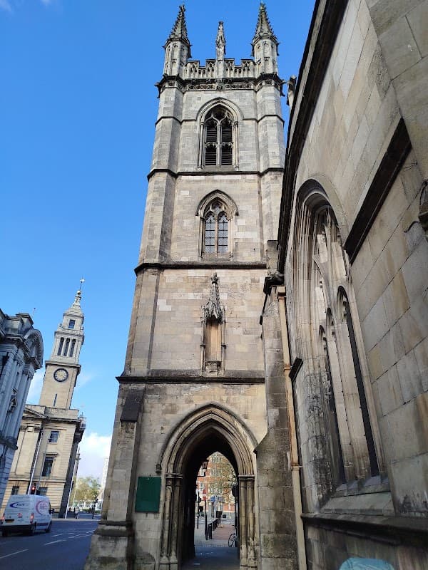 Tall stone tower with gothic architecture, flanked by buildings and a clear blue sky in Hanover Square, Hull.