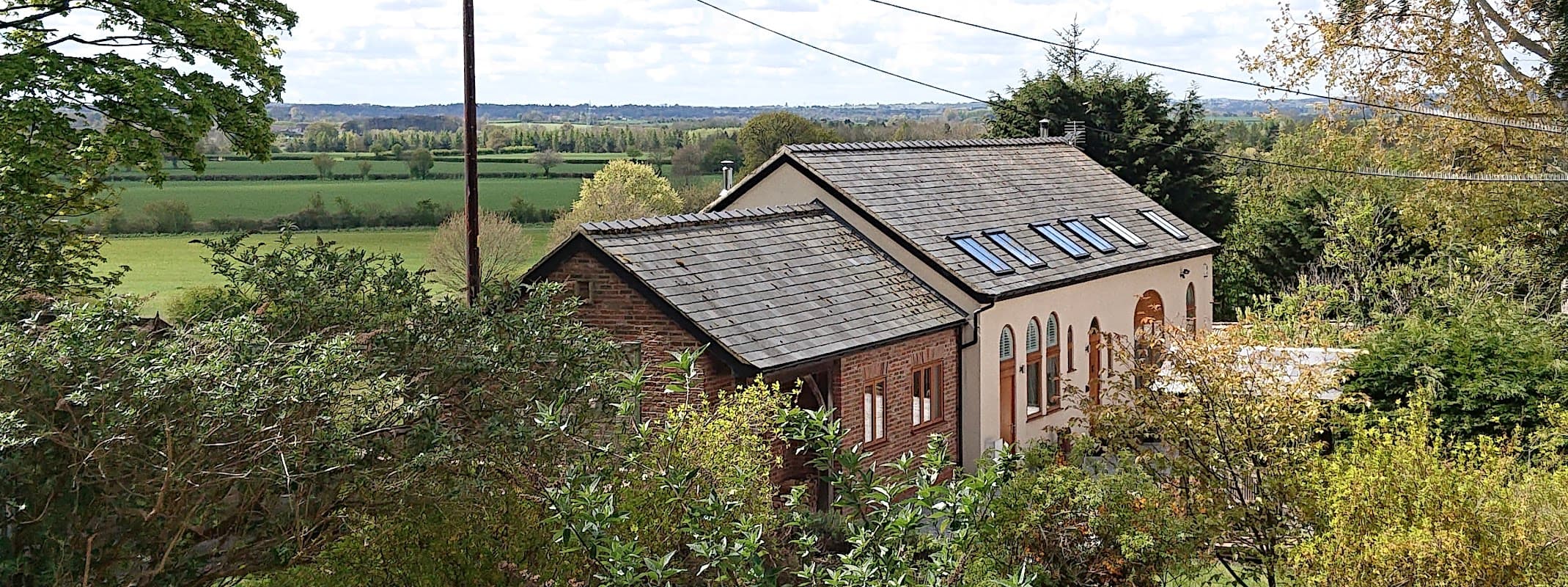 Glebe House holiday home with a sloped roof, surrounded by greenery and overlooking expansive fields in Hunsingore, Yorkshire.