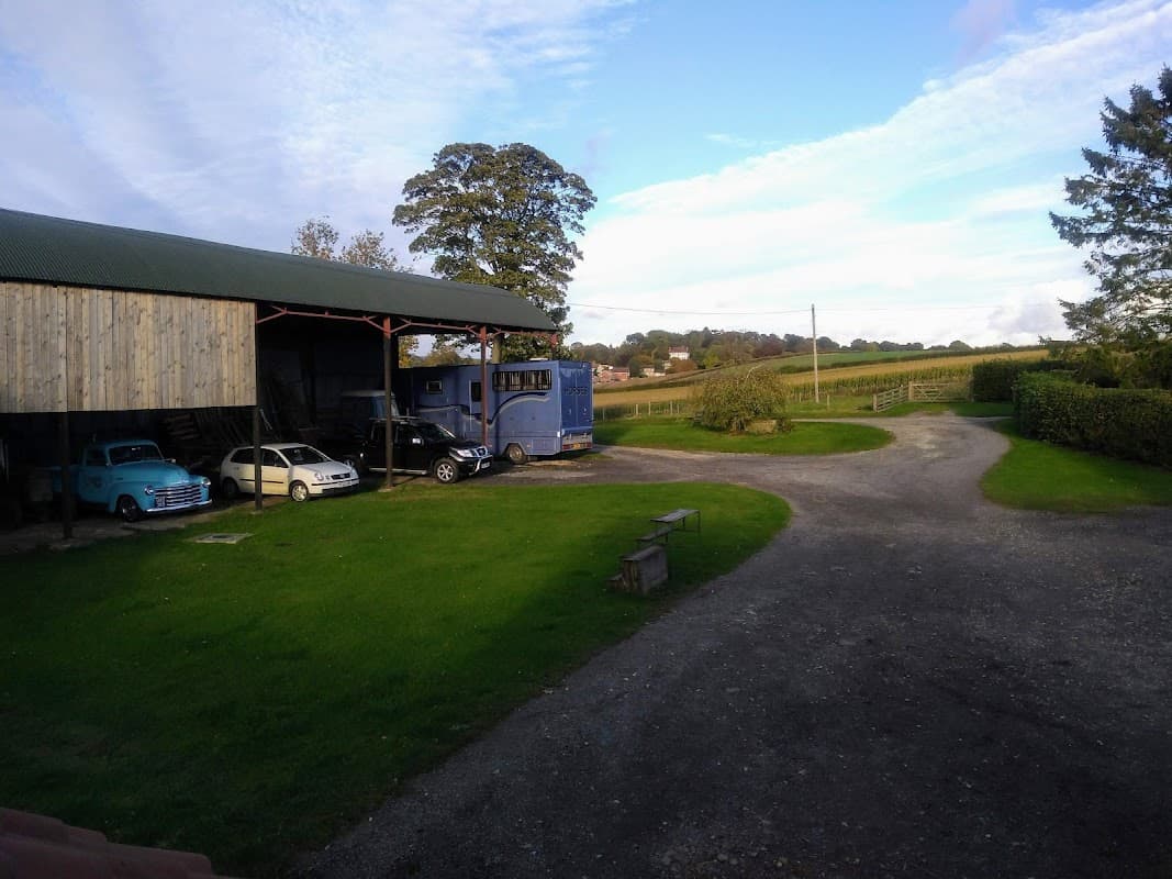 Charming farm holiday cottage with a blue truck, vintage cars, and lush green fields under a clear sky.