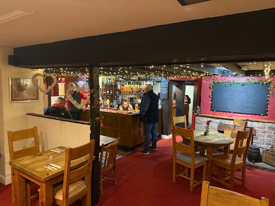Cozy bar interior with wooden tables, a counter stocked with drinks, and festive lights adorning the ceiling.
